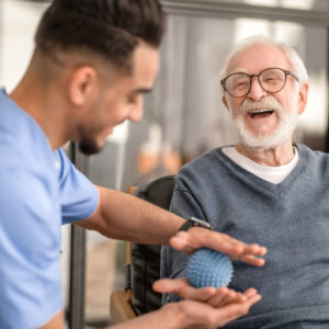 Joyous aged man undergoing a session of physical therapy conducted by an experienced rehabilitation doctor