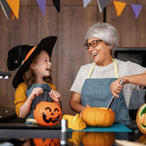 Happy family preparing for Halloween. Grandmother and granddaughter carving pumpkins at home.