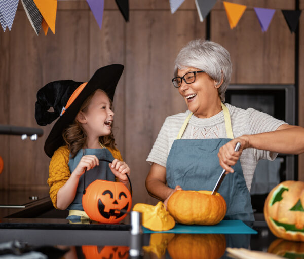 Happy family preparing for Halloween. Grandmother and granddaughter carving pumpkins at home.